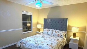 Ein Schlafzimmer mit einem Bett, zwei Nachttischen mit Lampen, einem Deckenventilator und einem Fenster mit Jalousien.