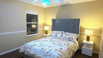 A bedroom with a bed, two bedside tables with lamps, a ceiling fan, and a window with blinds.