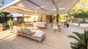 Un patio al aire libre con muebles de madera, una zona de estar cubierta y plantas en macetas.