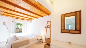 Un dormitorio con techo de madera, una cama con ropa de cama blanca, una mesita de noche con lámpara, un espejo y una ventana pequeña.