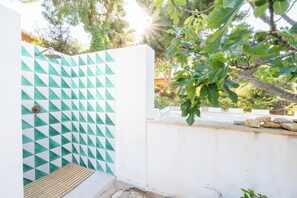 Ein Duschbereich mit einem geometrischen Fliesenmuster, einer Holzbank und einer weißen Wand.