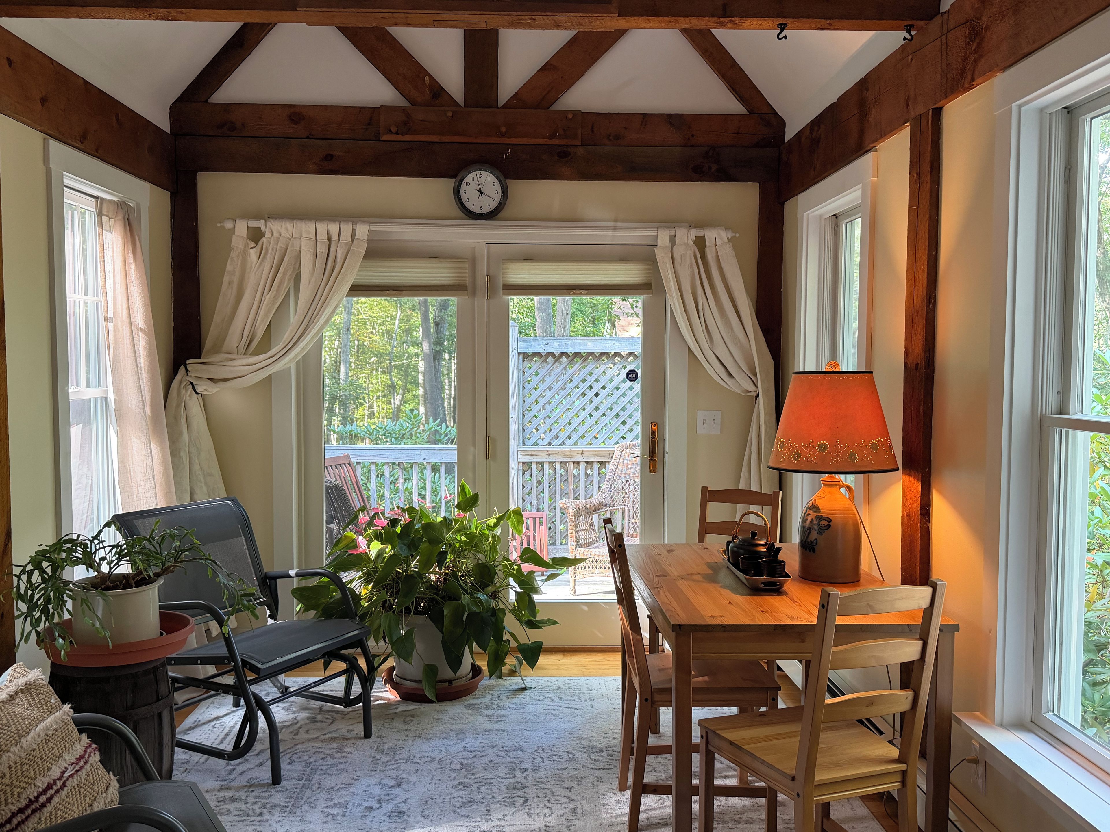 A cozy room with a wooden table, chairs, a potted plant, a clock, and a window with curtains.
