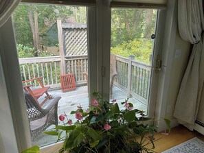A sliding glass door leading to an outdoor deck with a wooden railing, wicker chairs, and a potted plant with pink flowers. - Secluded 1-bedroom apartment in charming York (York)
