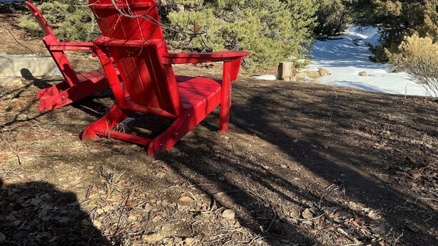 A red Adirondack chair in a natural setting with trees and a snow-covered hill in the background. - Welcoming 1-bedroom studio in vibrant Taos for your getaway (Taos)
