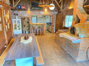 L’intérieur d’un chalet rustique comprend une table à manger en bois, un four en briques et un coin cuisine équipé d’un four à micro-ondes.