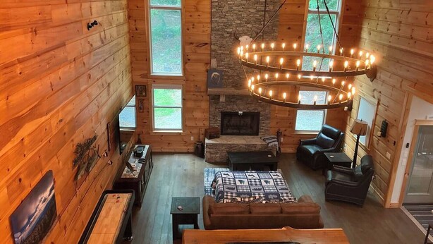 A cozy log cabin interior with a fireplace, wooden furniture, and large windows.