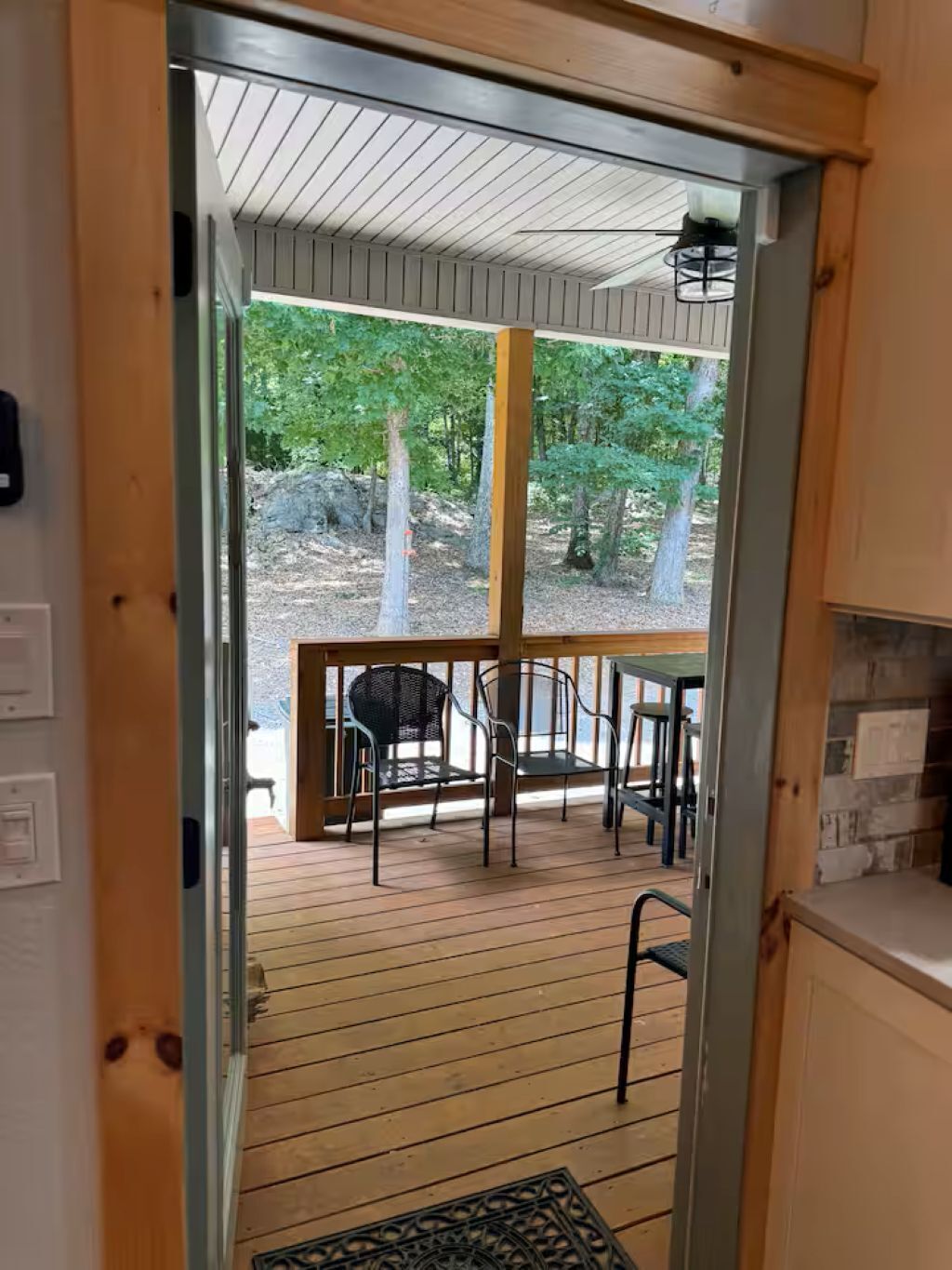 Eine Holzterrasse mit Tisch und Stühlen, die zu einem überdachten Außenbereich mit Bäumen führt.