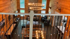 A wooden cabin interior with a loft area, a chandelier, and a stone wall.