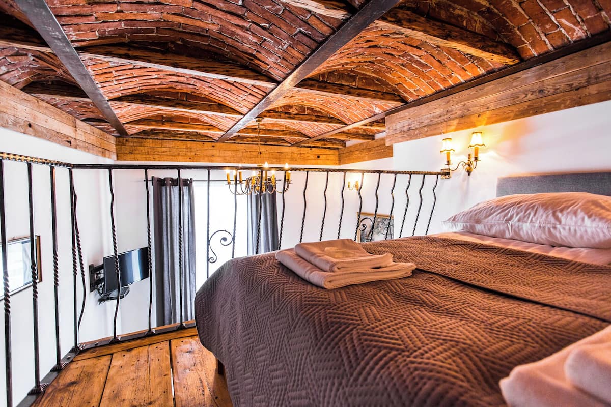 A bedroom with a rustic wooden ceiling, a bed with a brown textured blanket, and wall-mounted sconces.