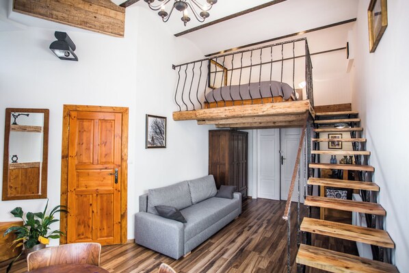 A loft-style room with a wooden staircase, a gray sofa, and a wooden door. - Lovenovsky Apartments (Krakow)
