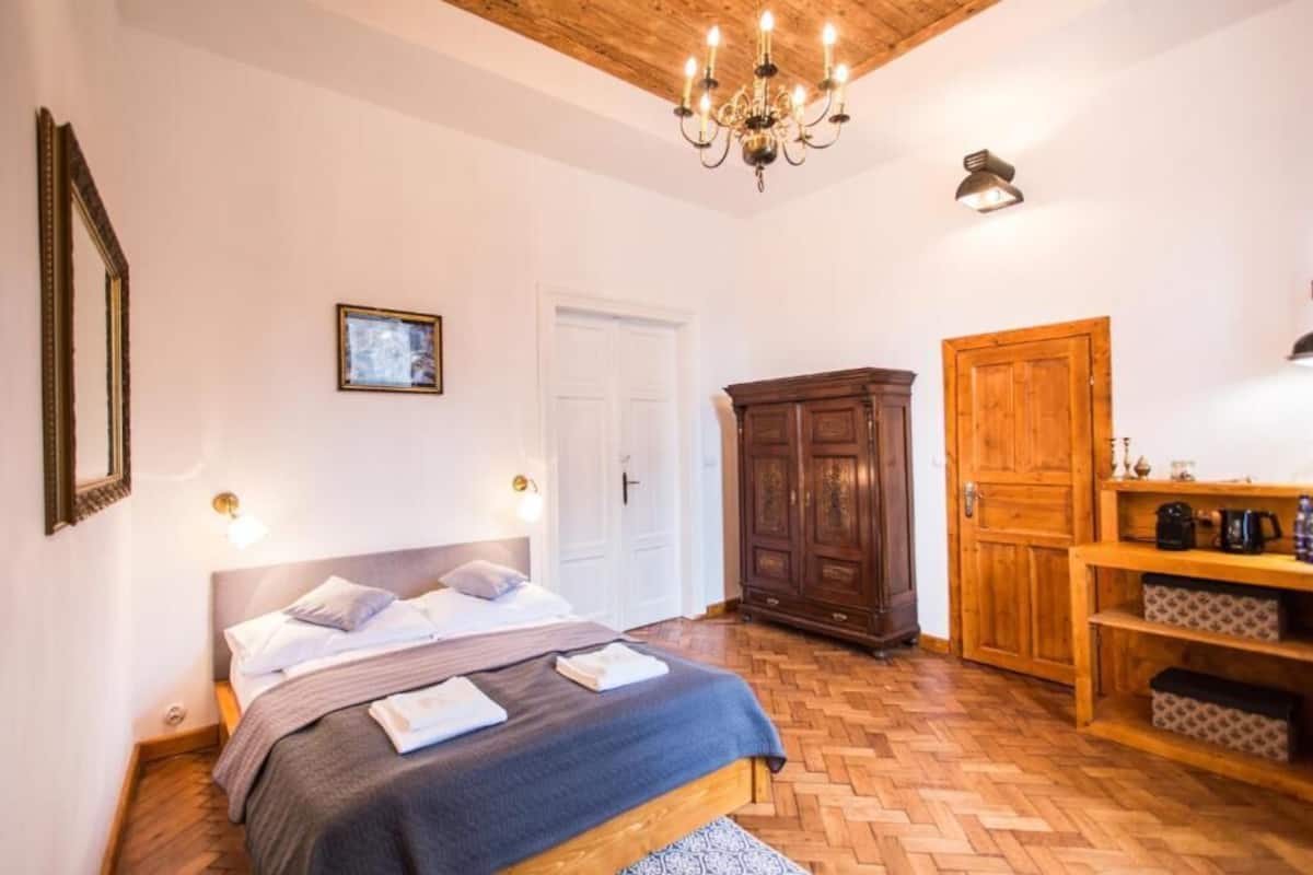 A bedroom with a bed, wooden wardrobe, and a chandelier.