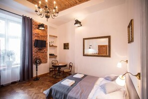 A room with a bed, a desk, a chair, a TV, a mirror, and a chandelier. - Lovenovsky Apartments (Krakow)