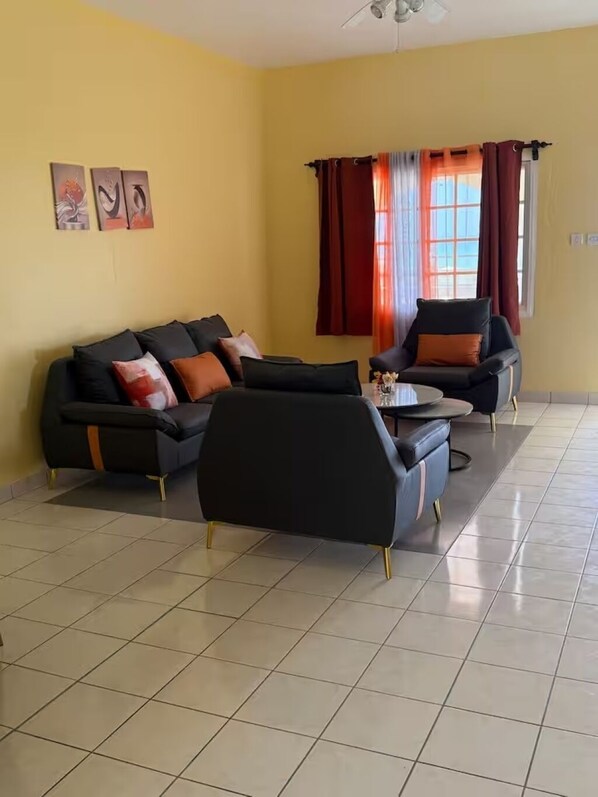A living room with a sofa, a coffee table, and two armchairs. There are three framed pictures on the wall. - Superstar Living - Room#01 with AC : Double bed with Balcony & sea view (Treasure Beach)