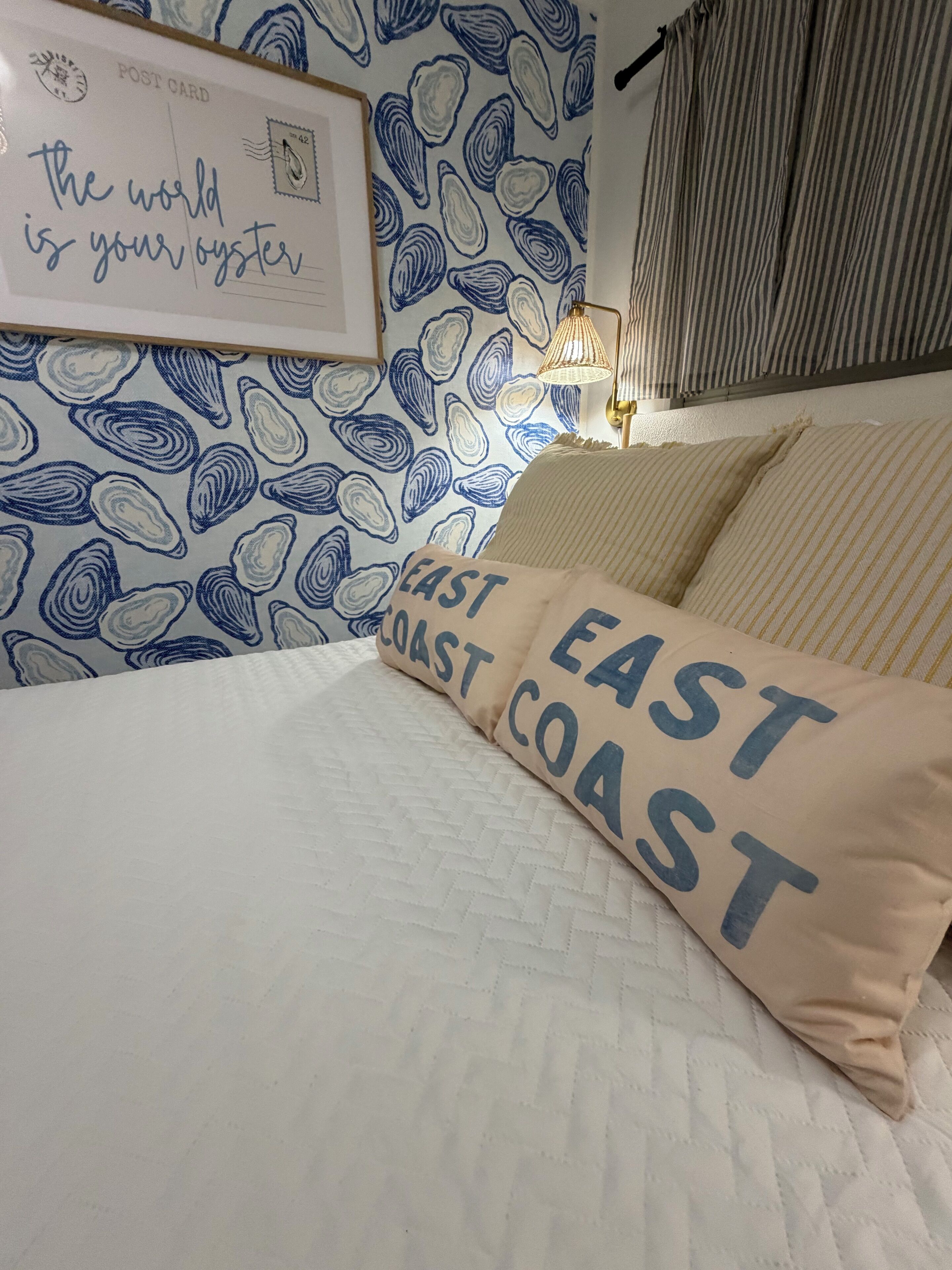 Ett sovrum med en säng, en vägg med ett blått och vitt mönster, en inramad citatbild och en kudde med texten ”EAST COAST”.