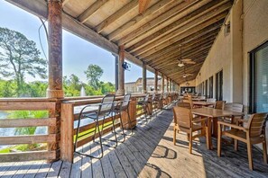 Ein überdachter Außenbereich zum Essen mit Holztischen und -stühlen, mit Blick auf ein Gewässer und viel Grün.