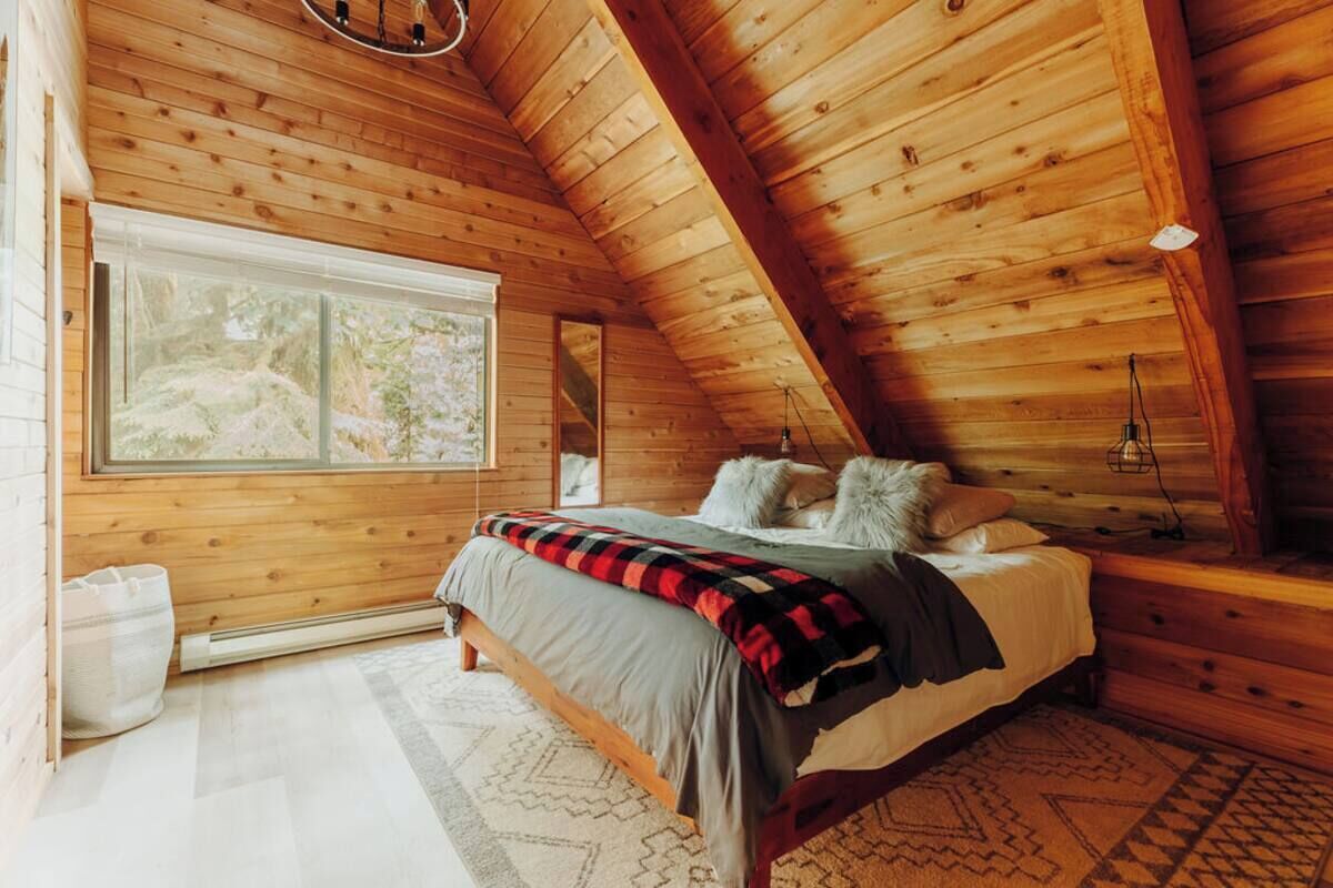 Um quarto aconchegante com teto de madeira, uma janela grande, uma cama com almofadas e um tapete.
