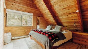 Um quarto aconchegante com teto de madeira, uma janela grande, uma cama com almofadas e um tapete.
