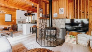 A cozy cabin interior with a stone fireplace, wooden walls, a kitchen area, and a flat-screen TV. - Zen Hideaway - Fiber - EV - King bed - Pet - Baker (Deming)
