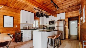 A modern kitchen with wooden cabinetry, a central island with stools, and hanging pots. - Zen Hideaway - Fiber - EV - King bed - Pet - Baker (Deming)