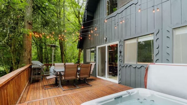 A wooden deck with a hot tub, outdoor furniture, and string lights. - Zen Hideaway - Fiber - EV - King bed - Pet - Baker (Deming)