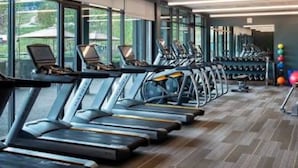 Una palestra con tapis roulant e attrezzature per esercizi, ampie finestre e pavimento rivestito di moquette.