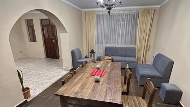 Een eethoek met een houten tafel en stoelen, een kroonluchter, een bank en een raam met gordijnen.