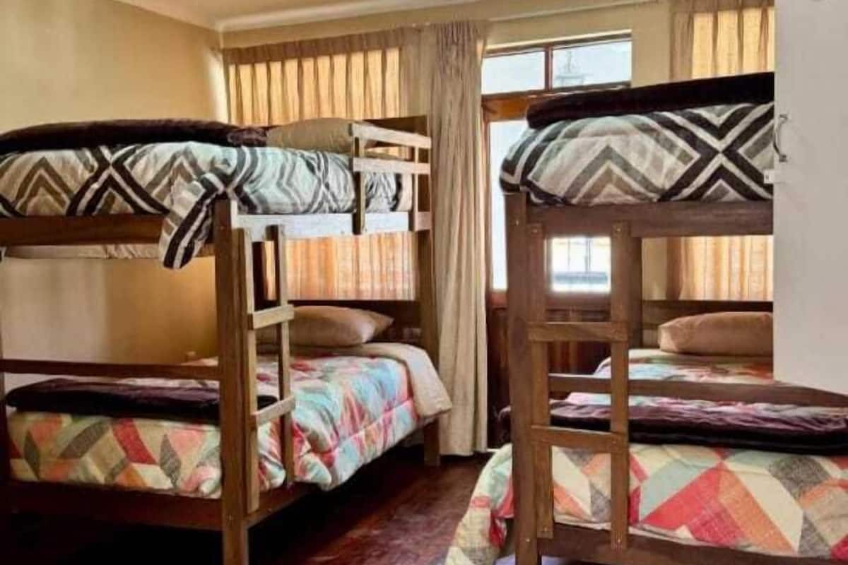 A dormitory room with bunk beds, wooden flooring, and a window with curtains.