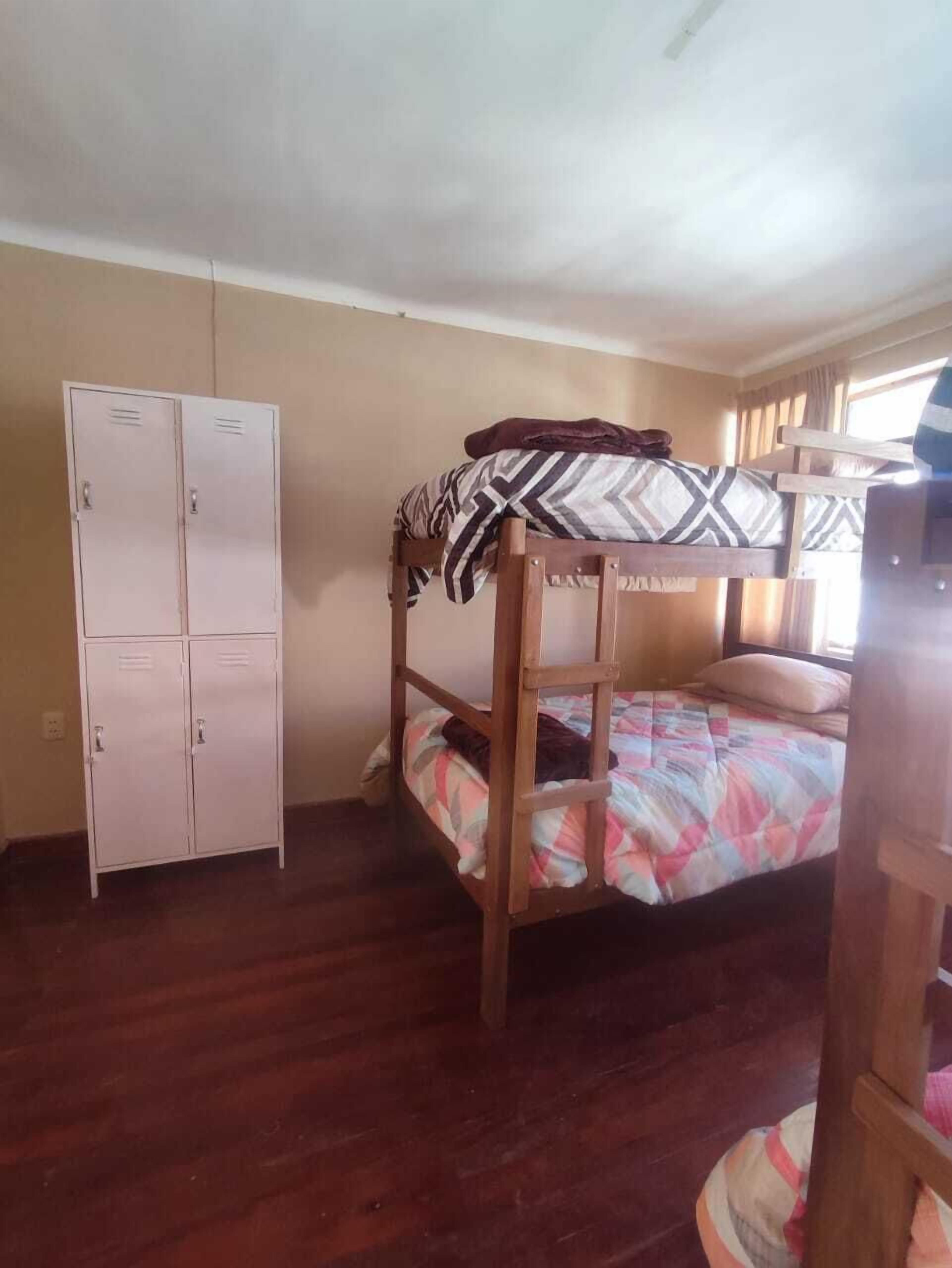 A bunk bed with a patterned blanket, a wooden wardrobe, and a window with curtains.