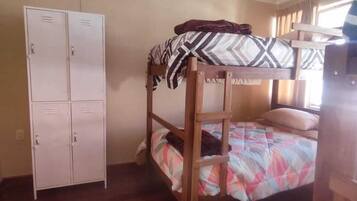 A bunk bed with a patterned blanket, a wooden wardrobe, and a window with curtains.