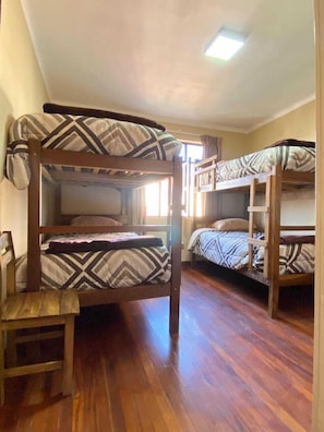 A bunk bed room with a wooden floor, a chair, and a window with curtains. - Santa Teresa Alley Hostel (Sucre)