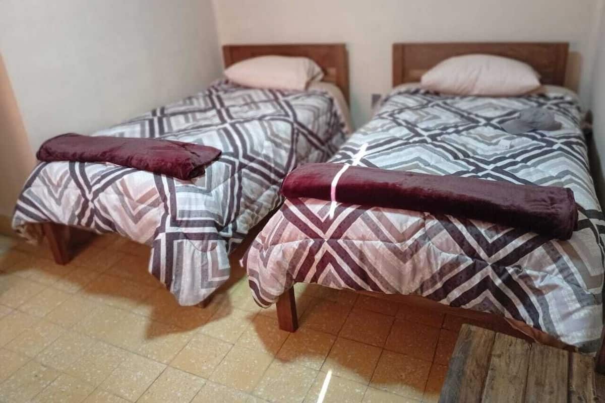 Two single beds with patterned bedding and wooden headboards in a room with tiled flooring.