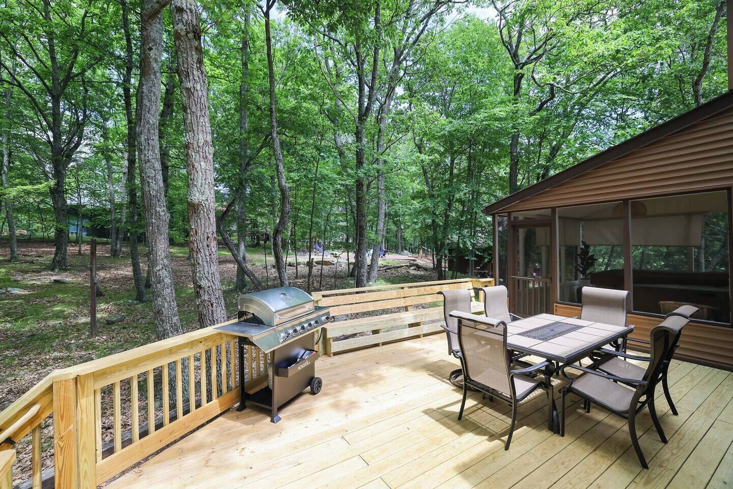 An outdoor deck with a grill, seating, and a view of the forest.