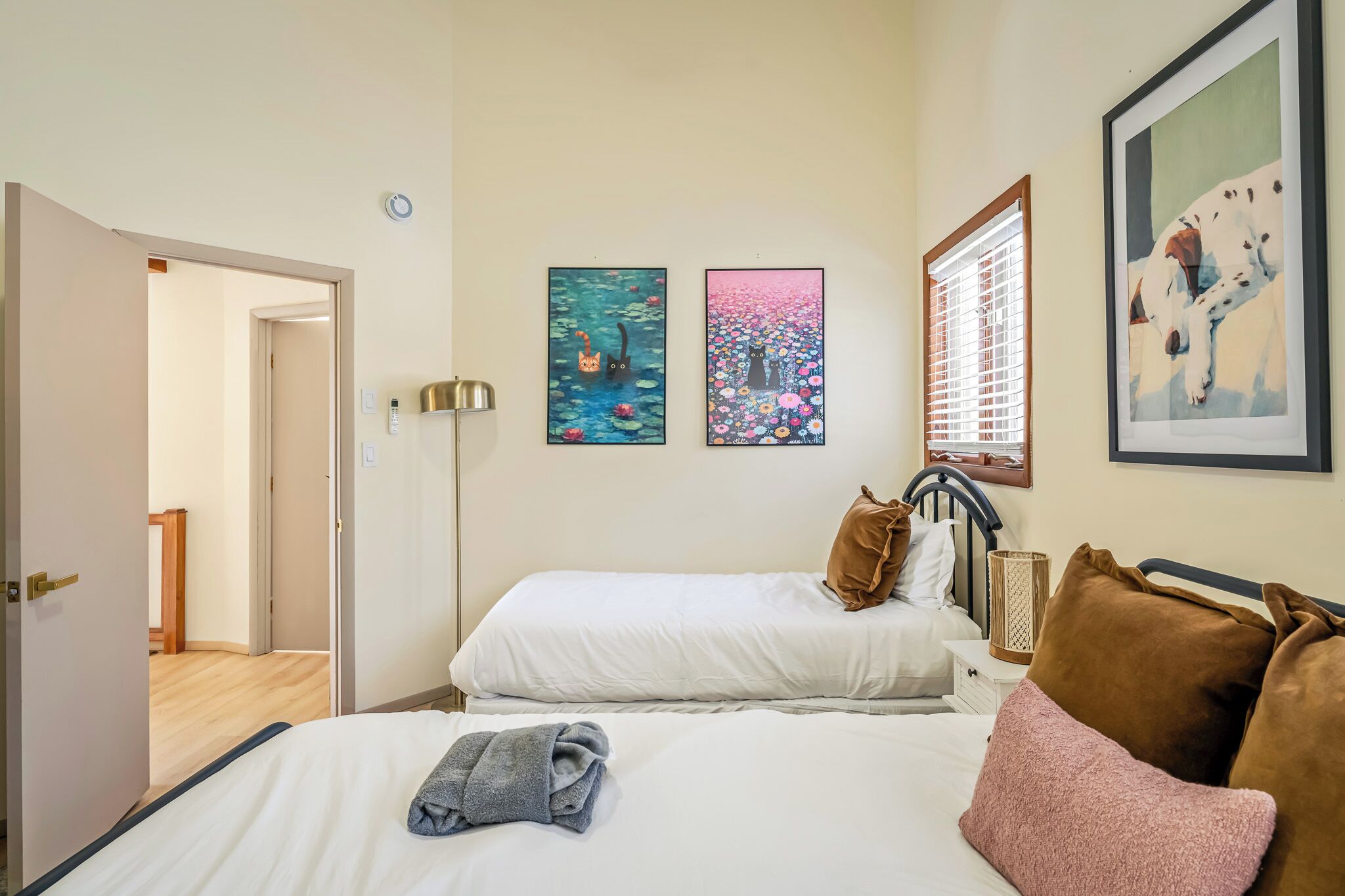 Camera d'albergo con due letti, una porta che dà su un'altra stanza e due quadri appesi alle pareti.