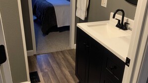 Ein Badezimmer mit einem weißen Waschbecken, schwarzen Schränken, einem Spiegel und einem Handtuch an der Wand.