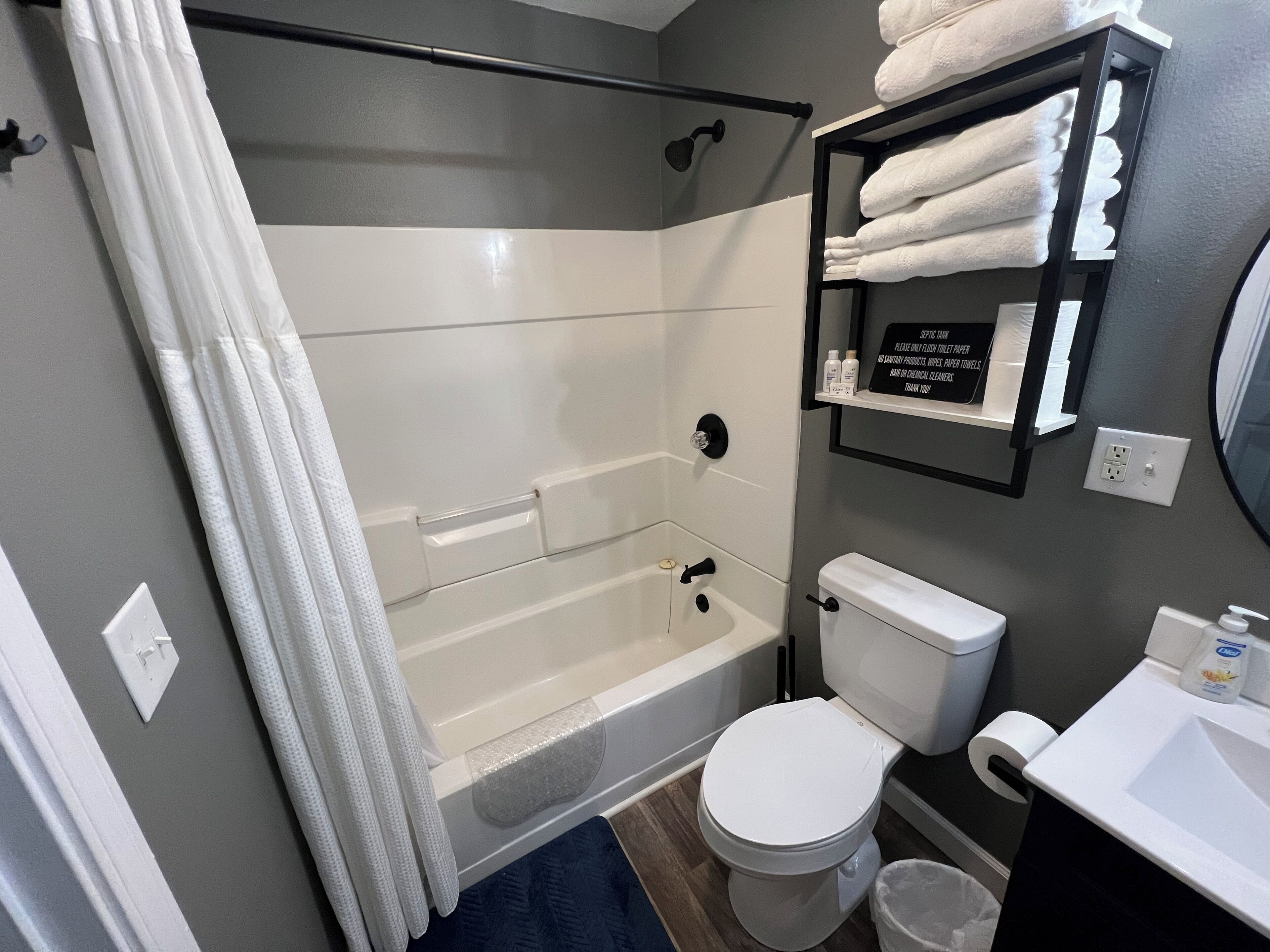 A modern bathroom with a bathtub, toilet, and a shelf with towels.