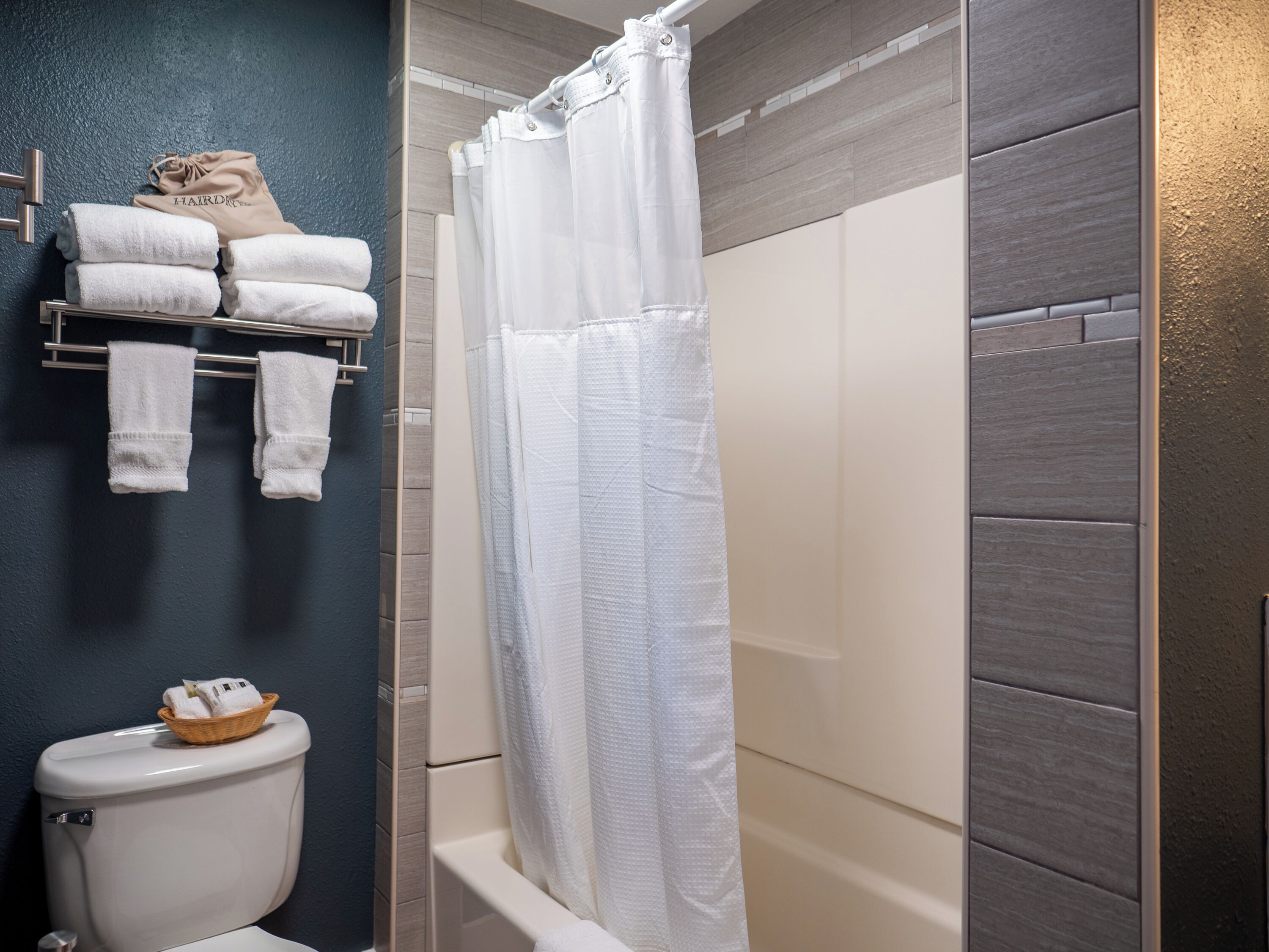 A bathroom with a toilet, a shower with a white curtain, and a towel rack with folded towels.