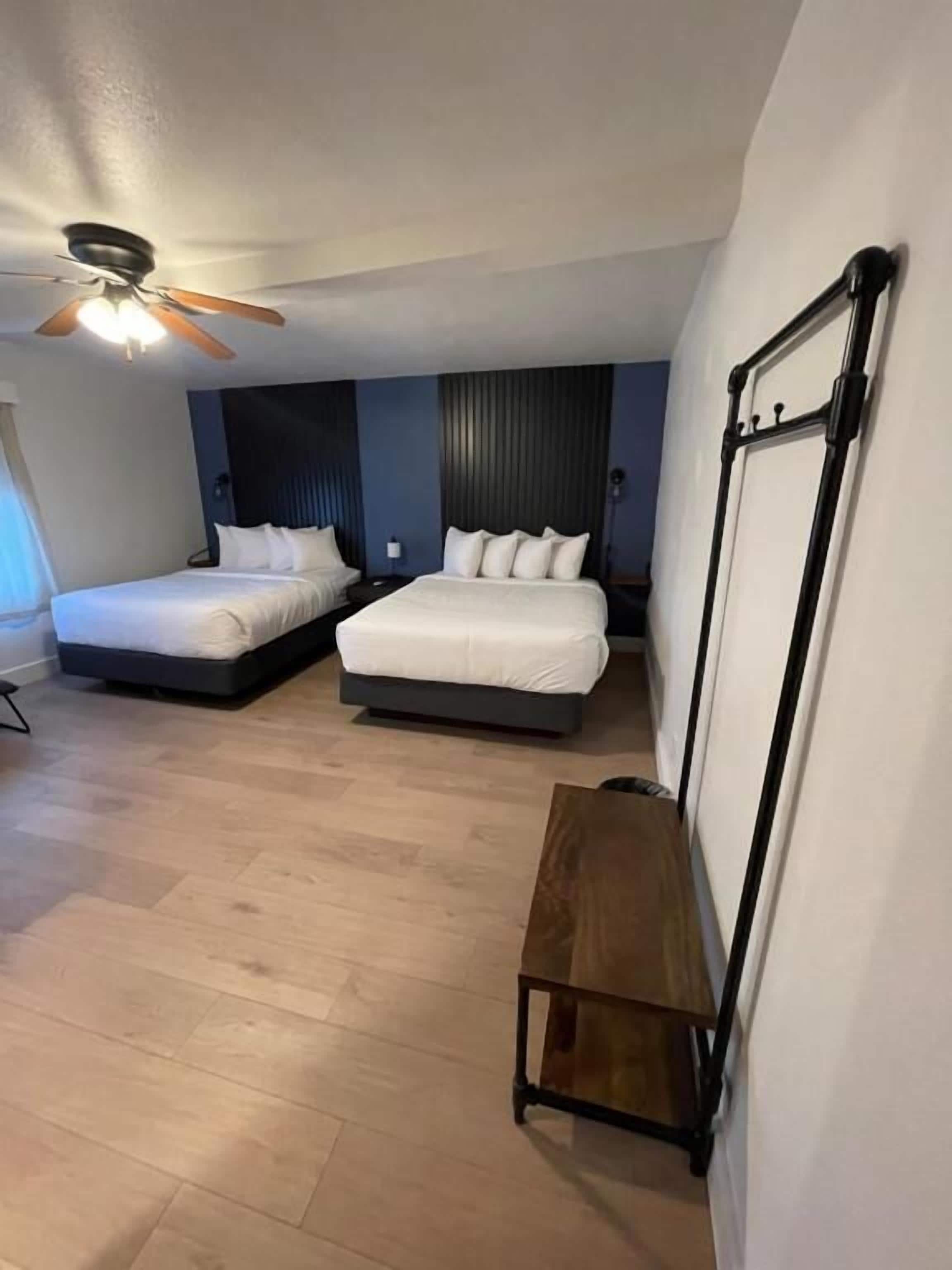 Una camera d'albergo con due letti, una ventola a soffitto, una panca di legno e una lavagna a parete.
