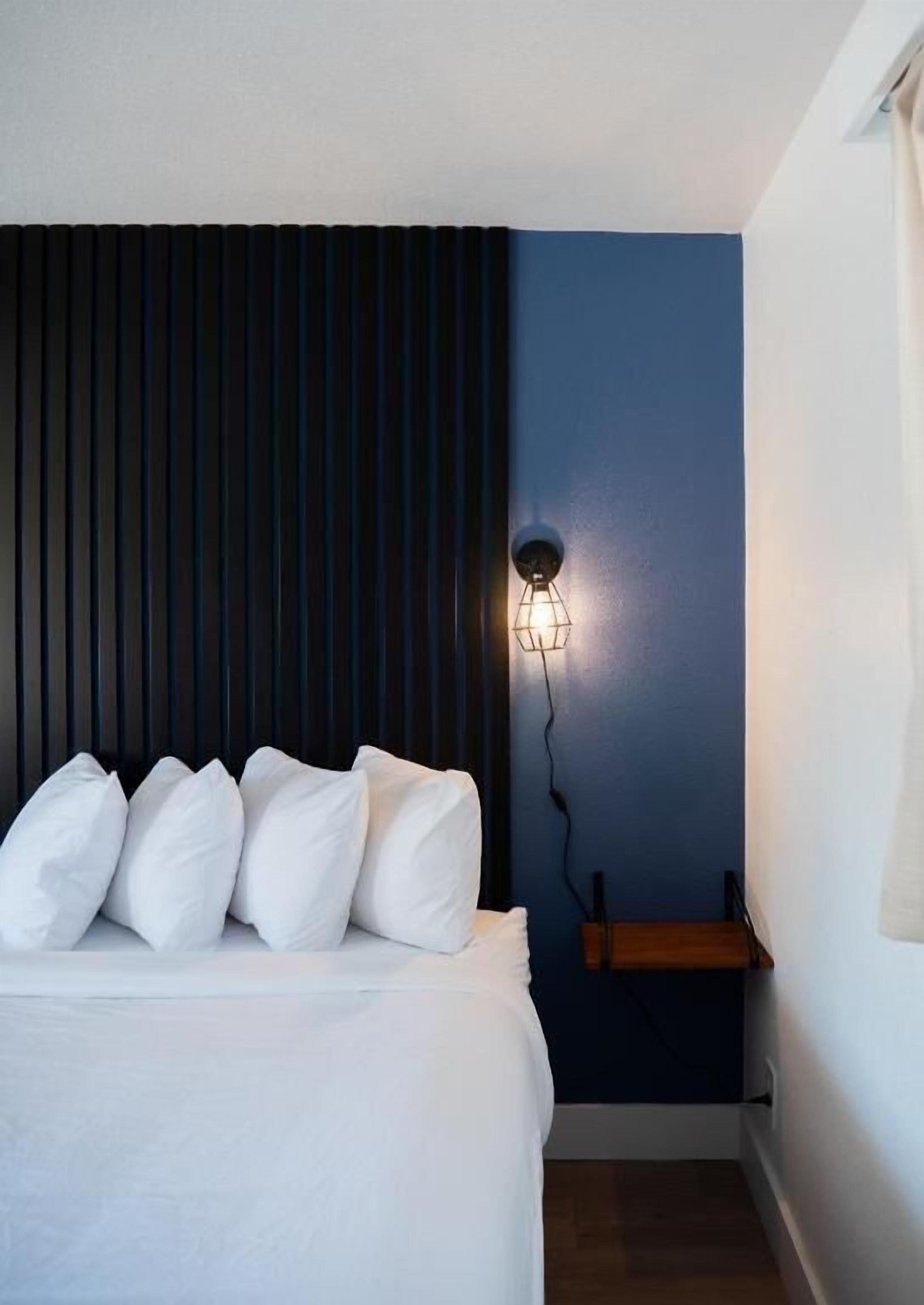 Ein Schlafzimmer mit einem Bett, einer Wandleuchte und einer hölzernen Sitzbank.