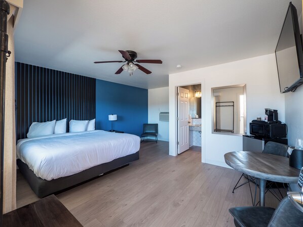 A modern hotel room with a large bed, a ceiling fan, a dining area with a table and chairs, and a kitchenette with a microwave. - Balanced Rock Inn (Fruita)