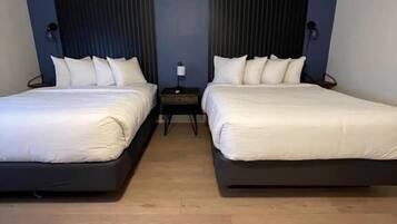 A hotel room with two beds, a nightstand, and a lamp.
