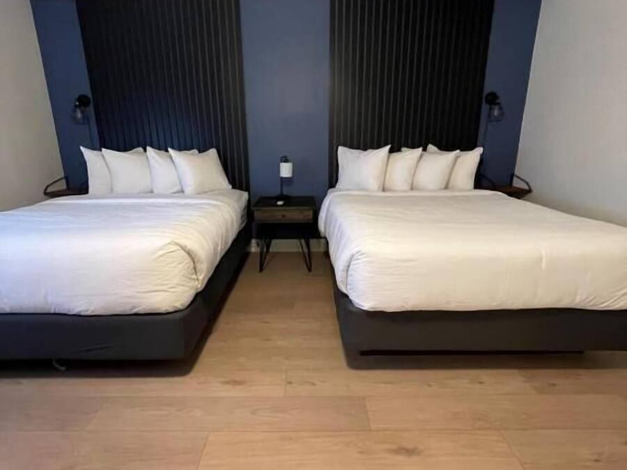 A hotel room with two beds, a nightstand, and a lamp.