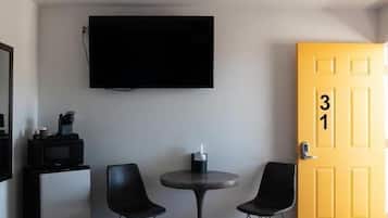 Habitación de hotel con una cama, un escritorio con televisor, dos sillas, un ventilador de techo y una puerta marcada con el número 31.