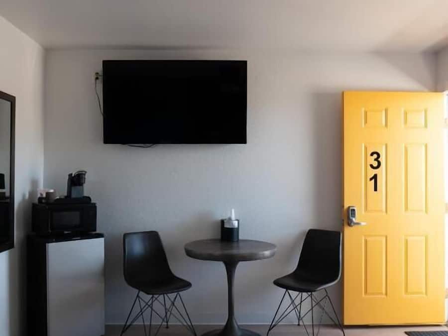 Habitación de hotel con una cama, un escritorio con televisor, dos sillas, un ventilador de techo y una puerta marcada con el número 31.