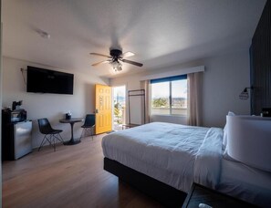 A hotel room with a bed, a desk, a chair, a TV, and a balcony with a view.