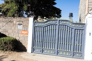 A gated entrance with a security sign, a stone wall, and a tree in the background.
