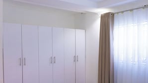 Ein Schlafzimmer mit großem Kleiderschrank, einem Bett und einem Fenster mit Vorhängen.