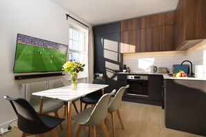 A modern kitchen with a dining area, a TV mounted on the wall, and a vase with flowers on the table. - Luxury duplex with 3beds/3baths. 15mins to Arsenal FC and Camden Town & Market (London)