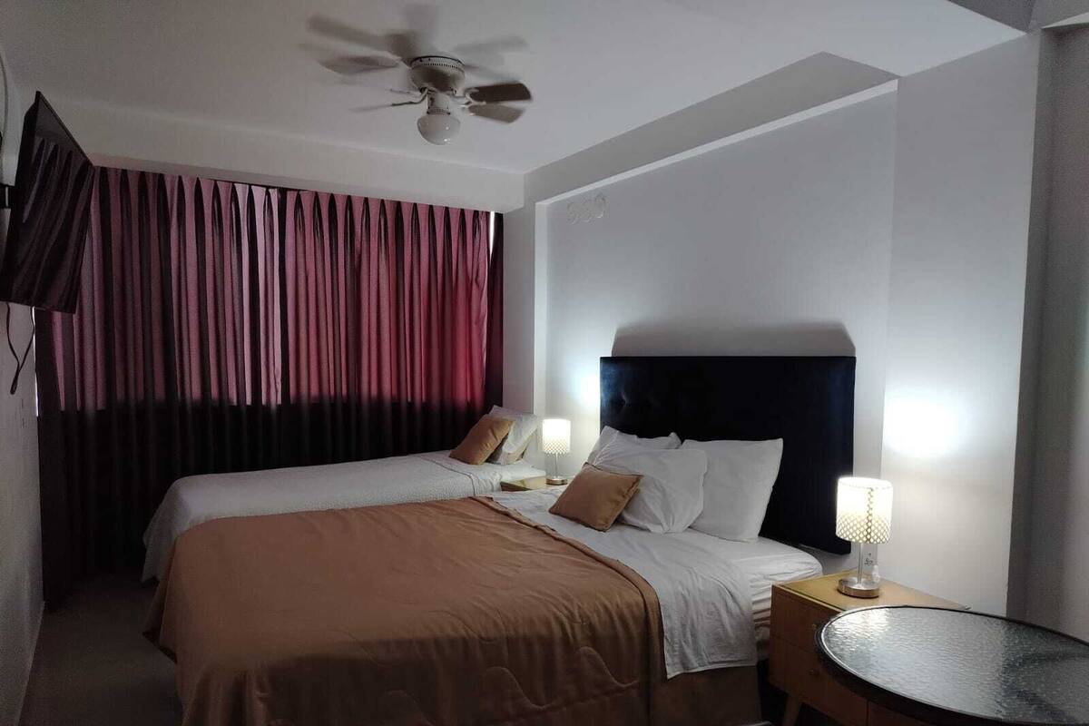 A hotel room with two beds, a ceiling fan, a round table, and a lamp.