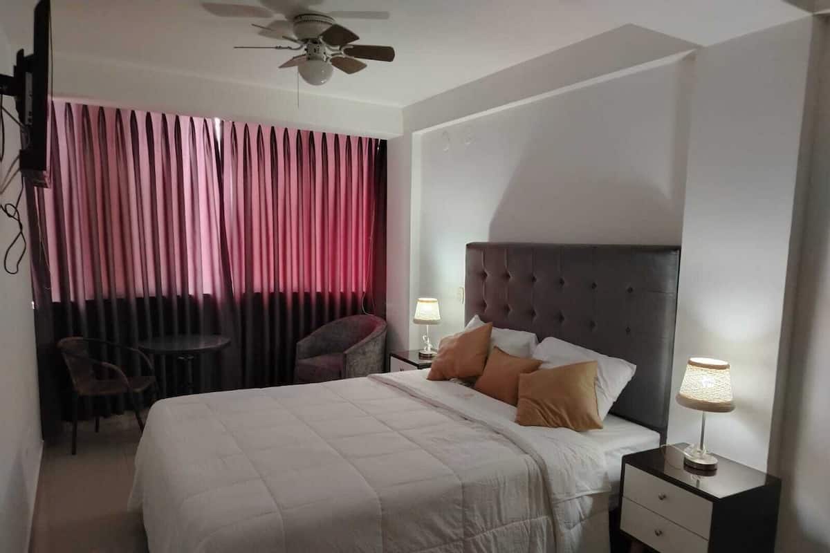 A hotel room with a bed, two bedside tables, a chair, a small table, and a ceiling fan.