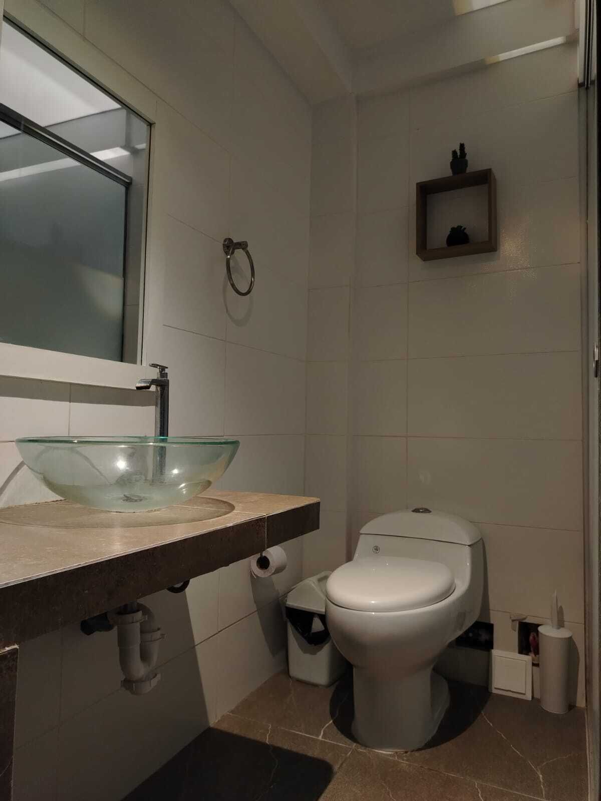 A bathroom with a glass bowl sink, a toilet, and a small shelf with a decorative item.